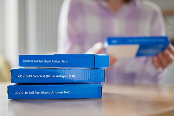 photo of a woman with a stack of at-home covid test boxes on her table