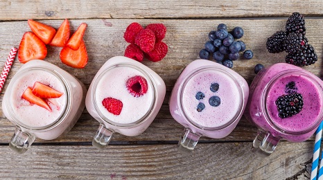 row of four mason jars with smoothies and fresh berries