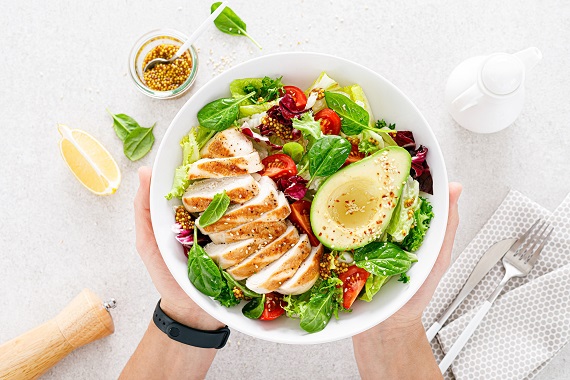 photo of someone holding a bowl of salad topped with grilled chicken and avocado