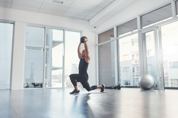 man doing a lunge and overhead press in an open gym loft space