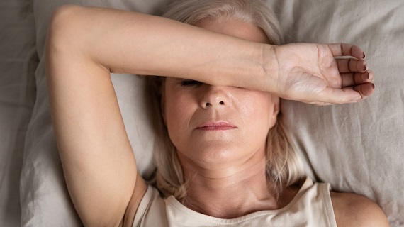 tired woman lying in bed touching her forehead