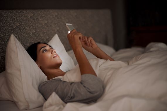 woman lying in bed looking at her smartphone