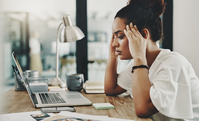 stressed young woman sitting at computer while rubbing her temples