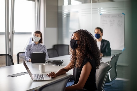 three people sitting in a conference room wearing face masks