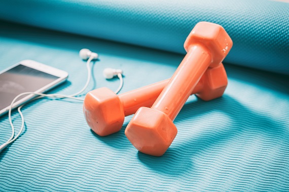 a pair of orange dumbells, a smartphone and earbuds on a yoga mat
