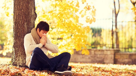 Sick patient blowing his nose by a tree.