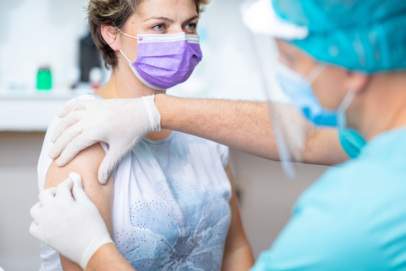 A healthcare provider prepares a masked patient for her flu shot.