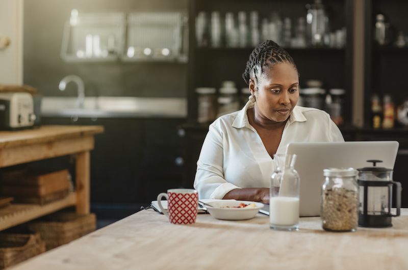 A woman sits at her kitchen table and researches at her laptop. 