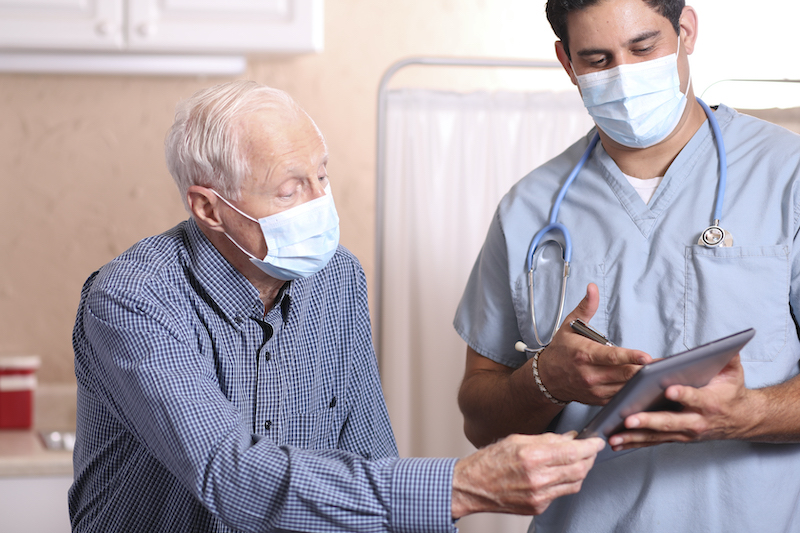 A masked doctor chats with his patient.