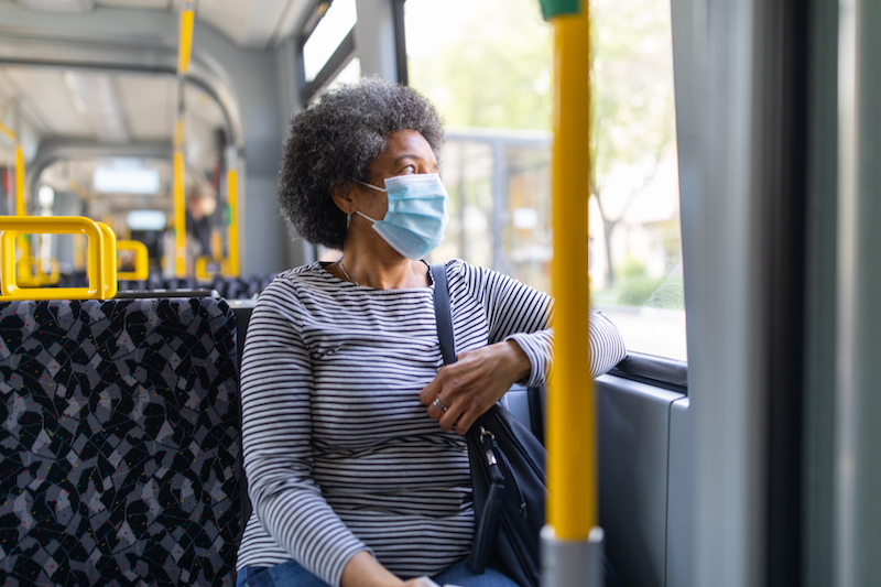 A masked woman rides a bus. 