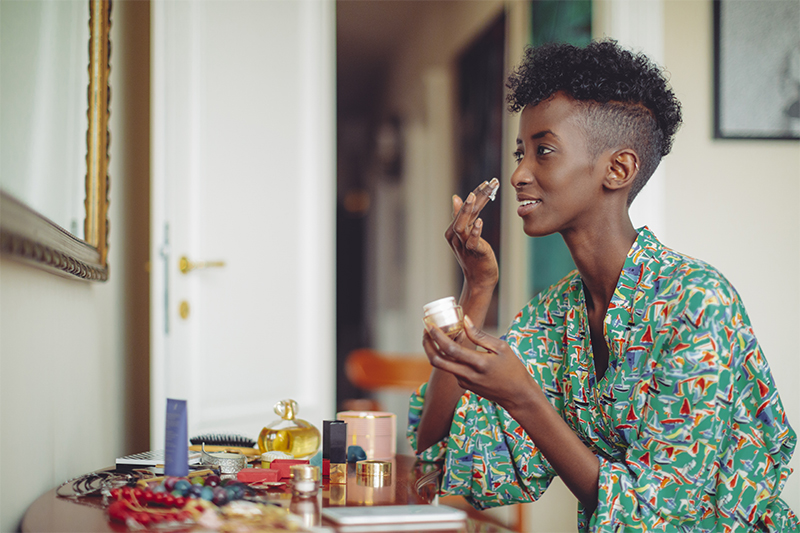 A woman applies moisturizer to her face.