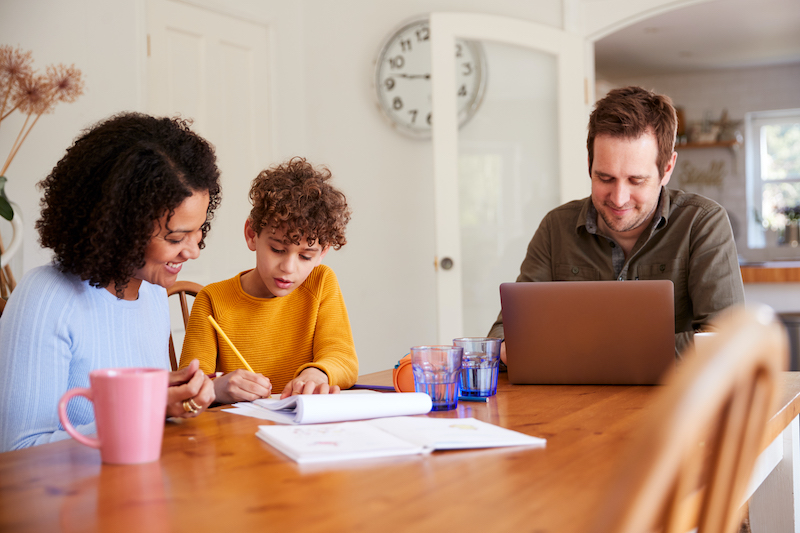 Two parents help their child with schoolwork at home. 