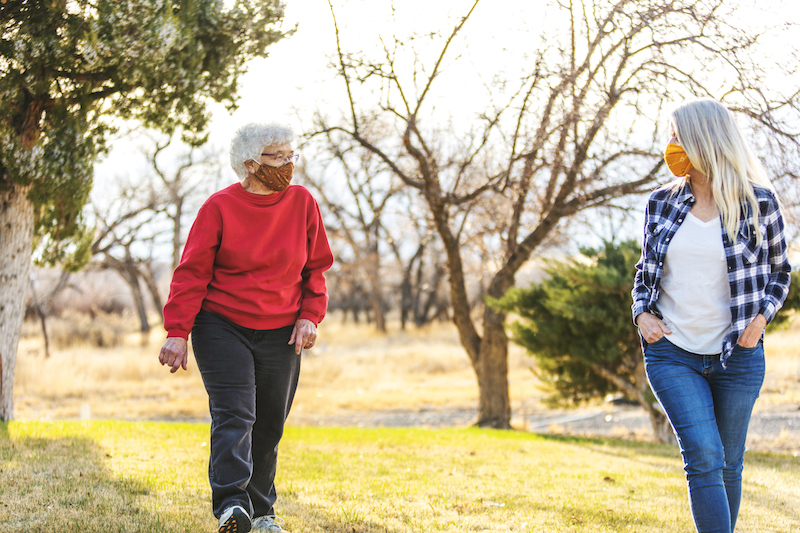 Two women maintain social distance while on a walk outside.