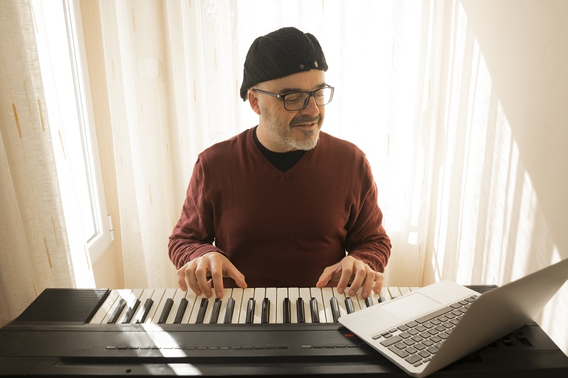 man learning to play the keyboard while looking at a laptop for instruction