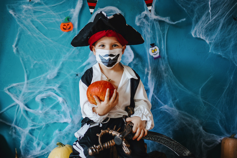 A young boy shows off his pirate Halloween costume and matching mask.