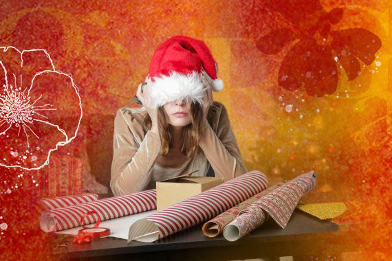 photo of woman in a Santa hat surrounded by wrapping paper with her head in her hands looking stressed