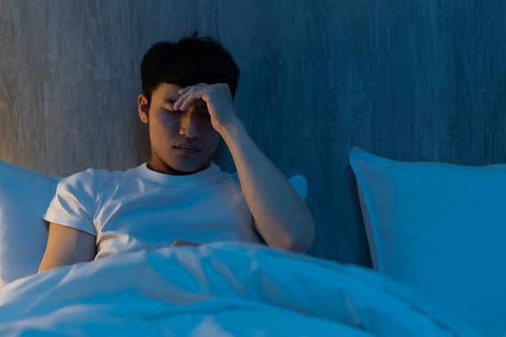 young man with insomnia sitting up in bed at night