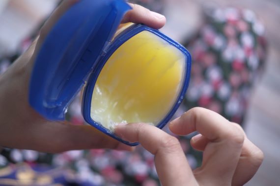 photo of a person dipping their finger into a tub of petroleum jelly