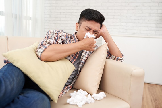 young man sitting on a couch blowing his nose