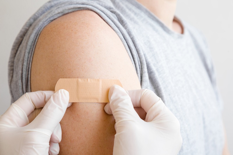 gloved hands applying a bandage to a patient's upper arm