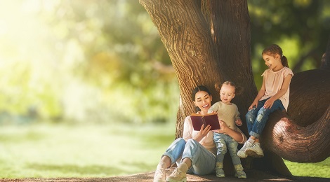 Family sitting and reading a book next to a tree.