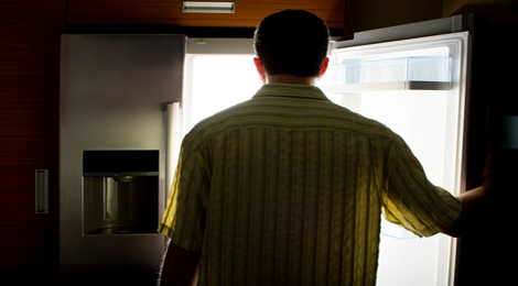 A man staring at his refrigerator in the middle of the night. 