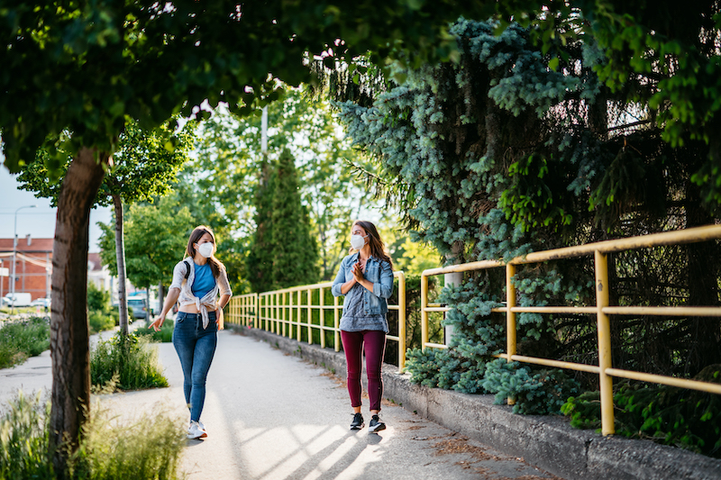 Two friends take a socially distanced walk while wearing masks.