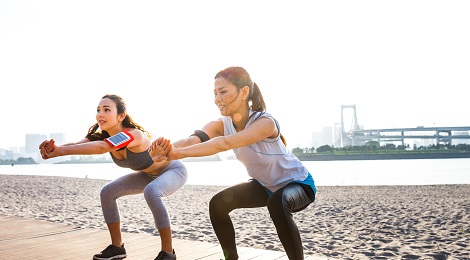 Two women doing squats by the beach. 